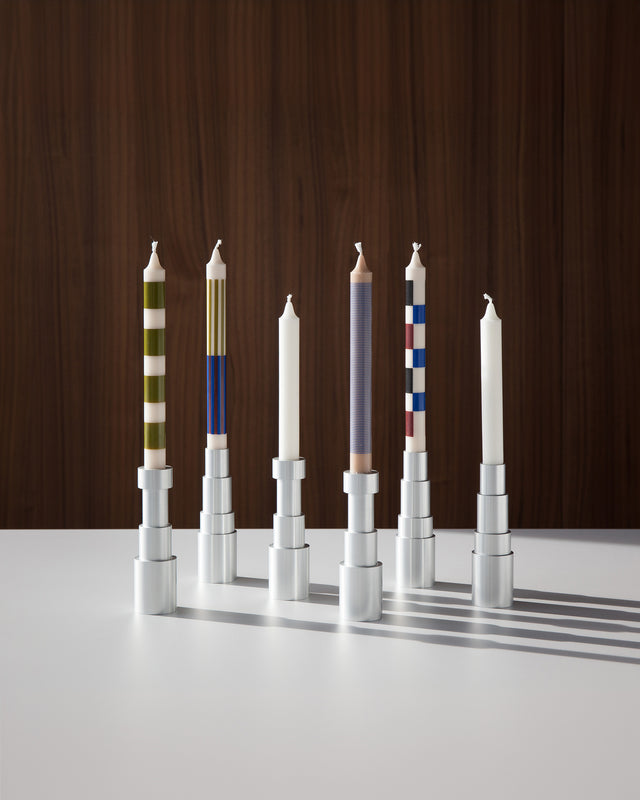 Modern aluminum candle holders with distinctive striped candles, arranged in a line on a pristine white table with a dark wood background
