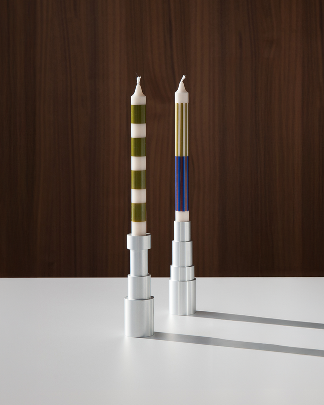 Modern aluminum candle holders with distinctive striped candles, arranged in a line on a pristine white table with a dark wood background