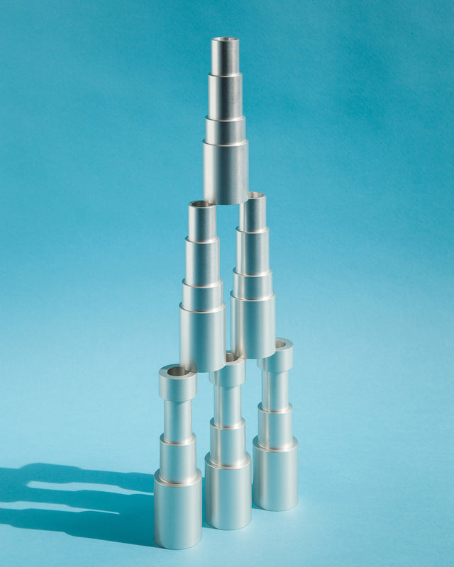 Abstract composition of aluminum candle holders displayed one on top of the other over a light blue background.