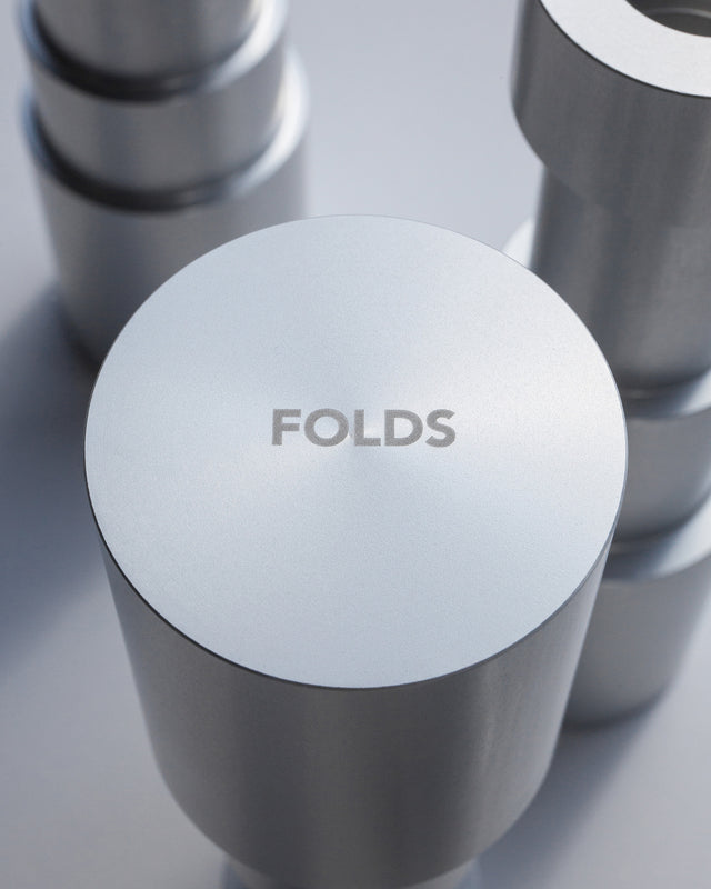 Close-up of the underside of a minimalist and pristine aluminum candle holder showcasing the FOLDS logo engraving and microstripes contributing to its manufacturing method.