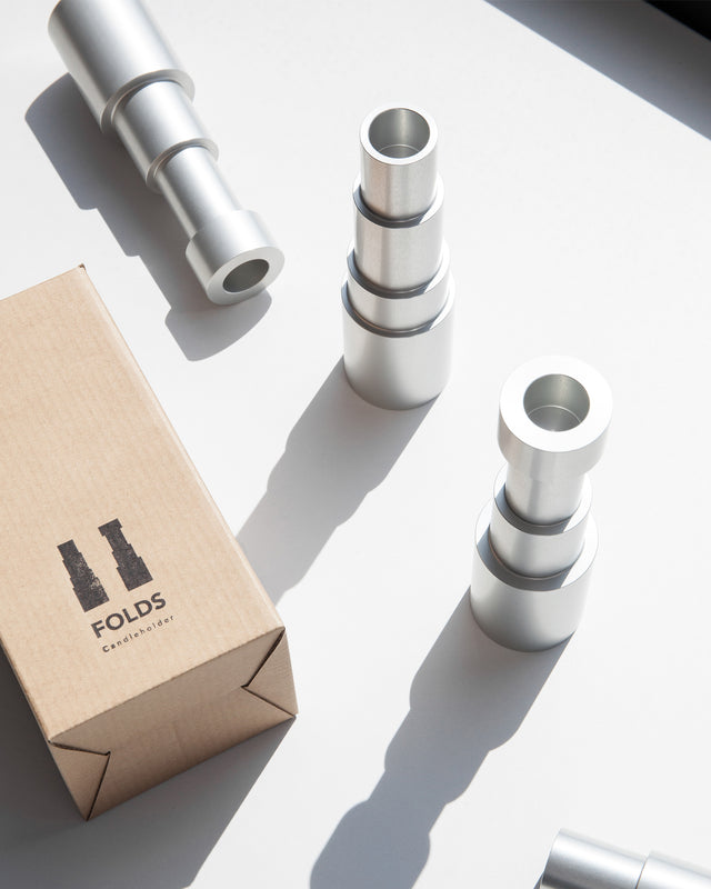 Close-up of modern aluminum candle holders next to their branded packaging, bathed in sunlight.